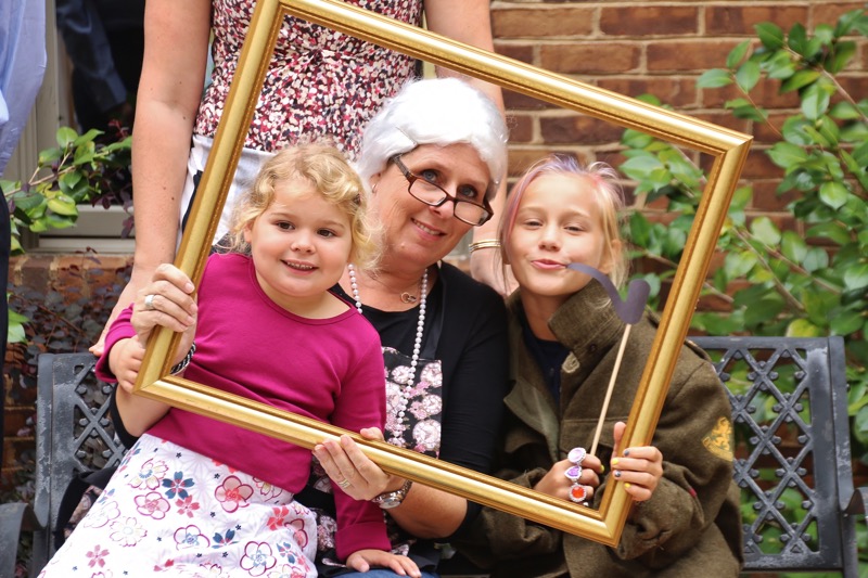 Photo of two children posing with a teacher dressed as a historical figure, holding up an empty photo frame as part of a school activity.